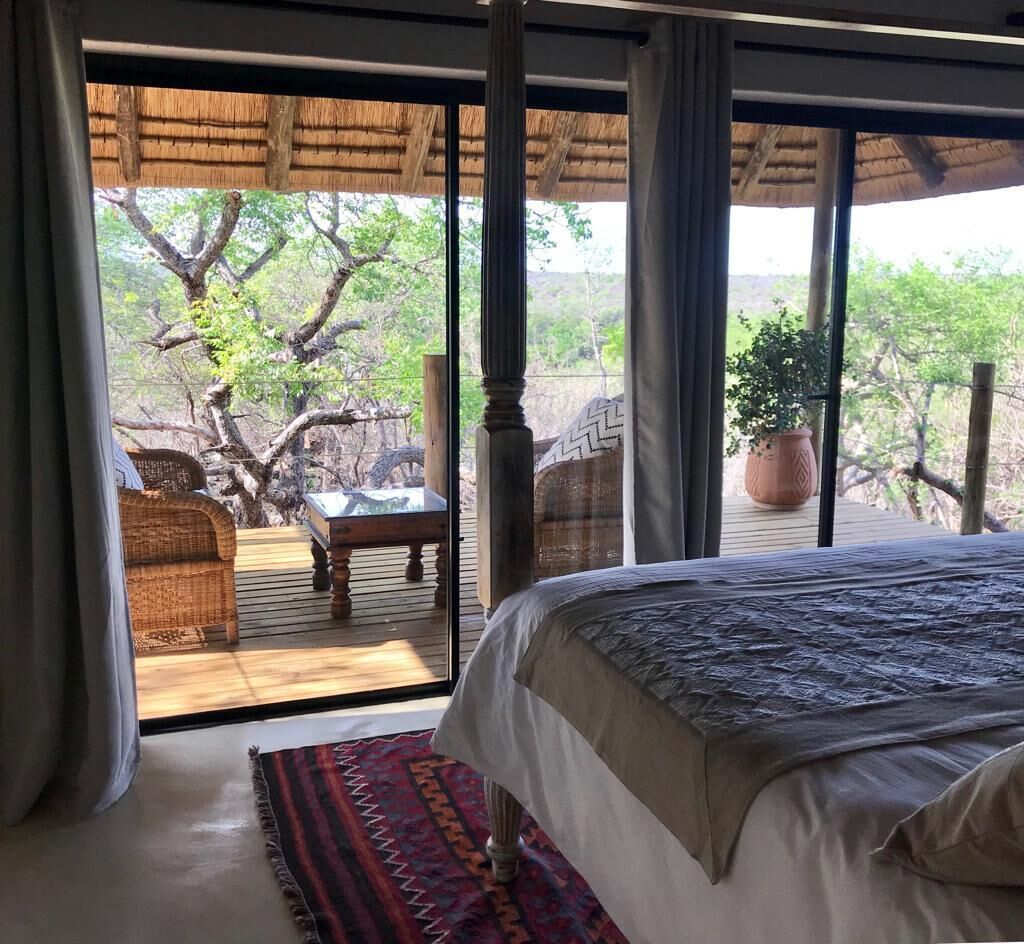 Un dormitorio con una cama grande, vistas al exterior y una terraza de madera con una silla y una mesa.