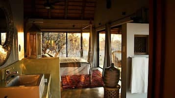 A bedroom with a large window, a bed, a bedside table, and a view of trees.