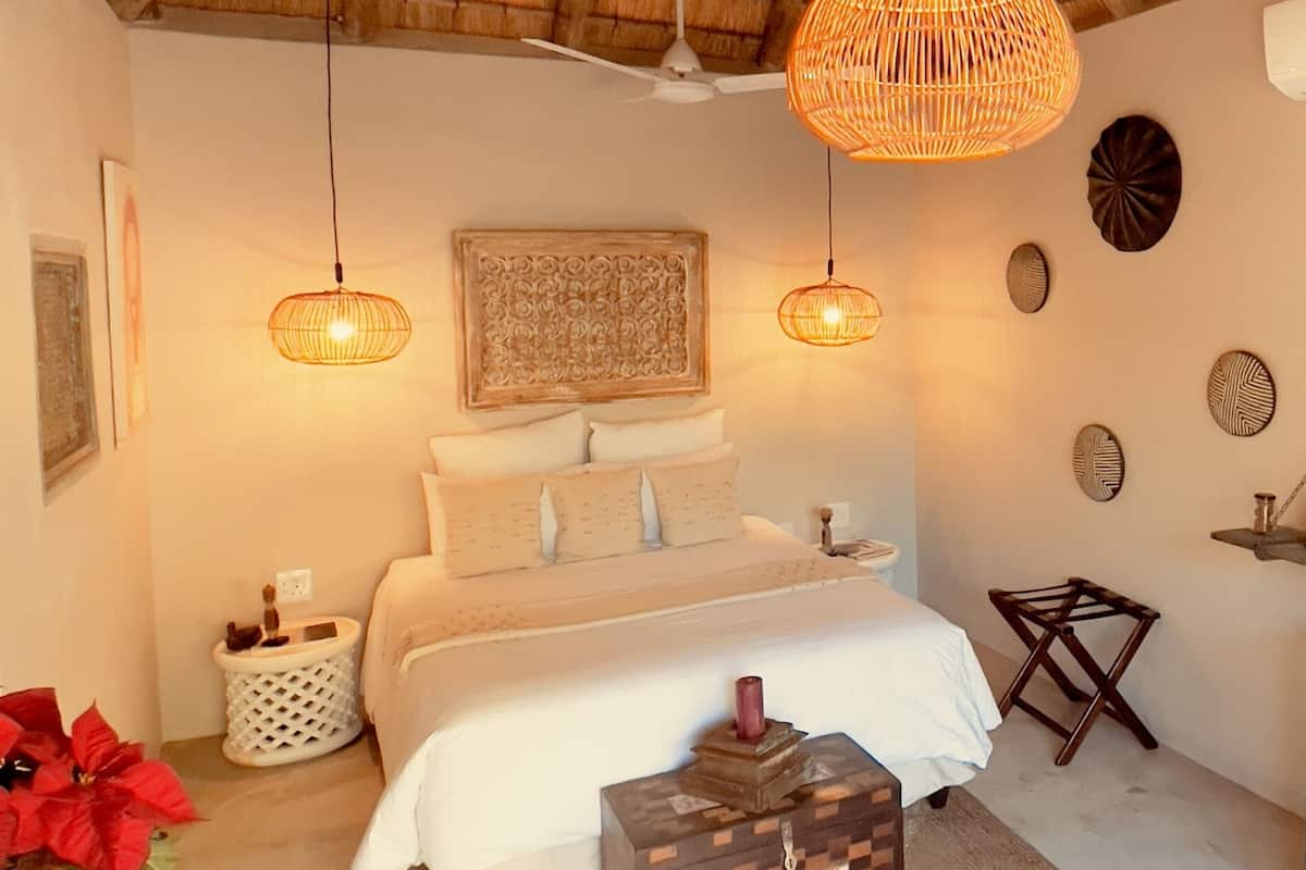 A bedroom with a bed, two hanging wicker lamps, a ceiling fan, a decorative wall piece, and a small wooden stool.