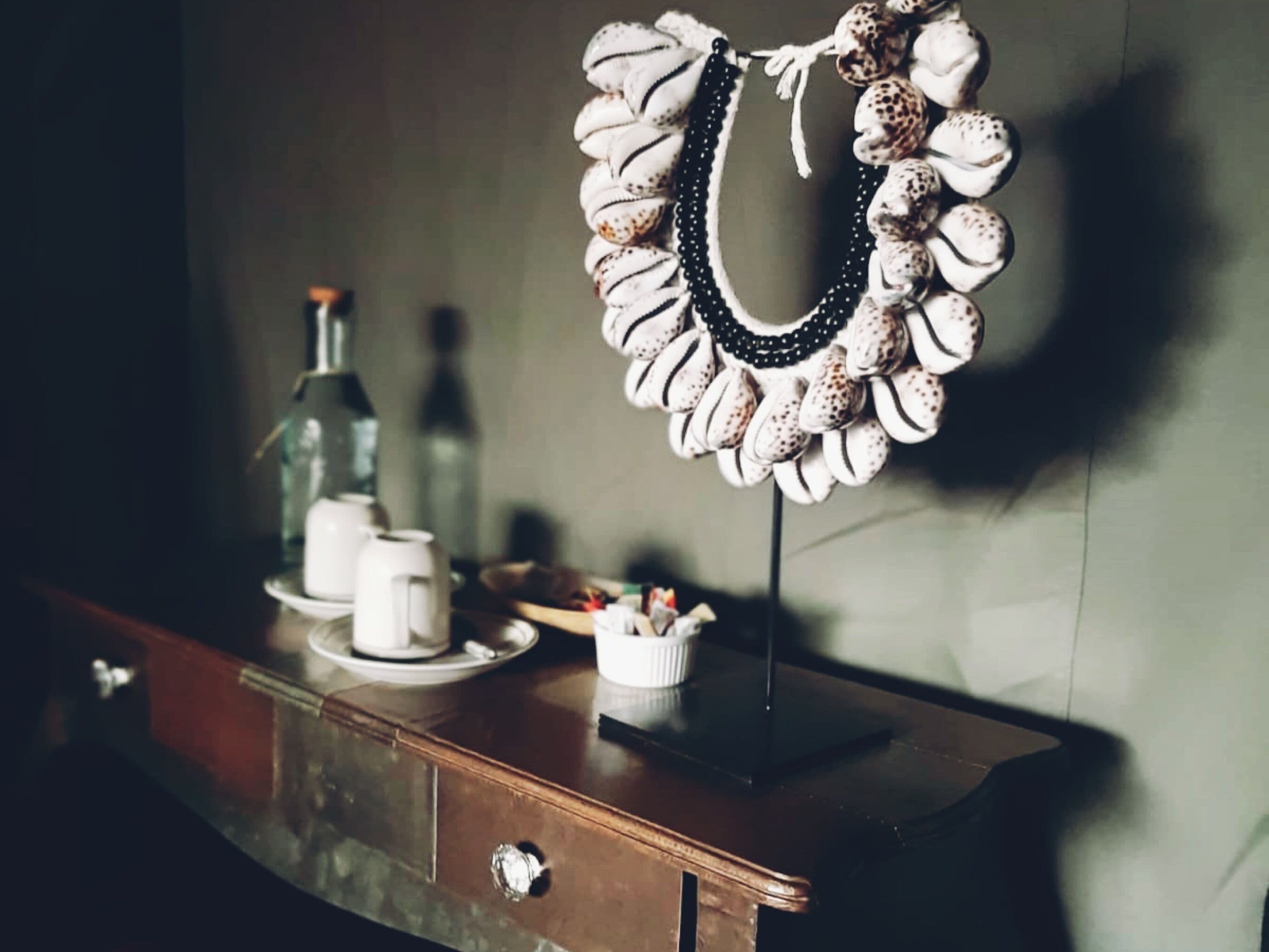 Une commode en bois avec un miroir, une petite tasse blanche et une bouteille.