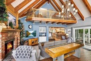 A spacious living room with a fireplace, a pool table, and a balcony with a wooden railing. - Storybook Lakefront: Luxury, Custom Built Lakefront Estate with Outdoor Hot Tub & Boat Dock! (Big Bear Lake)