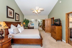 Een slaapkamer met een bed, een houten dressoir, een plafondventilator en ingelijste foto’s aan de muur.