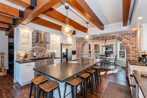 A spacious kitchen with a large island, wooden beams, and a brick accent wall.