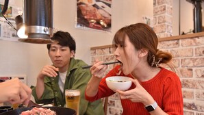 Uma pessoa comendo à mesa, com uma tigela, pauzinhos, uma panela com comida e uma caneca de cerveja.