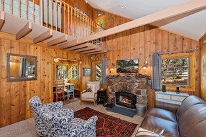 A wooden interior with a fireplace, a sofa, a patterned armchair, and a dining area.