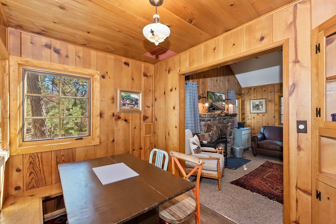 A wooden interior with a dining table, chairs, a fireplace, and a view of the outdoors.
