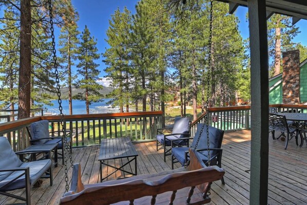 A wooden deck with outdoor furniture, overlooking a body of water and surrounded by trees.