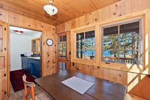 A wooden interior with a dining table, a clock, and a view of the outdoors.
