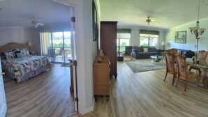 Een ruime woonkamer met balkon, een eetgedeelte met glazen tafel en een slaapkamer met groot bed en uitzicht op de omgeving.