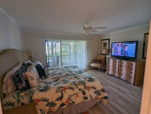 Ein Schlafzimmer mit einem Bett, einem Fernseher, einem Deckenventilator und einem Fenster mit Jalousien.