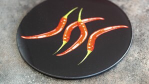 Une assiette noire sur laquelle reposent trois piments rouges, le tout posé sur une surface texturée.