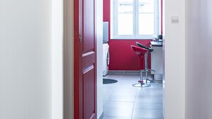 Un couloir avec une porte rouge, une fenêtre et deux tabourets de bar rouges.