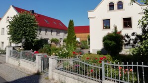 Ett bostadsområde med två vita hus, det ena med ett rött tak och det andra med ett vitt tak. Framför husen finns ett staket av metall med blommor.