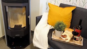 Ett modernt vardagsrum med en vedeldad kamin av märket Justus, en mörk soffa med en senapsgul kudde, en liten krukväxt, ett brickbord med en bok, en vinflaska och ett glas.