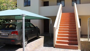A building with a car parked under a green umbrella, a staircase, and a door leading to an interior space. - Bell Rock 19 (Plettenberg Bay)