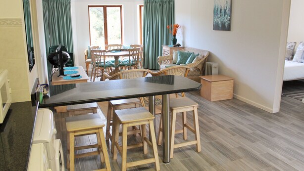 A spacious living area with a dining table, wooden stools, a sofa, and a radiator. - Bell Rock 19 (Plettenberg Bay)