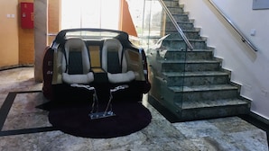 A car equipped with massage chairs in a hotel lobby, a staircase with glass railings, and a red fire alarm box.