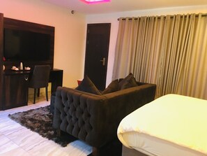 A hotel room with a bed, a sofa, a TV, a desk, and a door. - Ponte Vedra Hotel And Suite (Lagos)