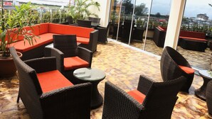 A rooftop terrace with wicker furniture, potted plants, and a view of the cityscape.