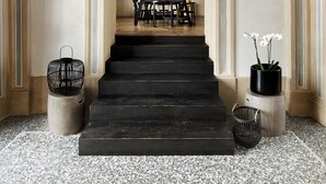A grand staircase with a black handrail, flanked by two black baskets and a potted plant.