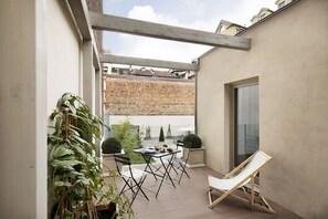 A balcony with a table and chairs, a lounge chair, and potted plants.