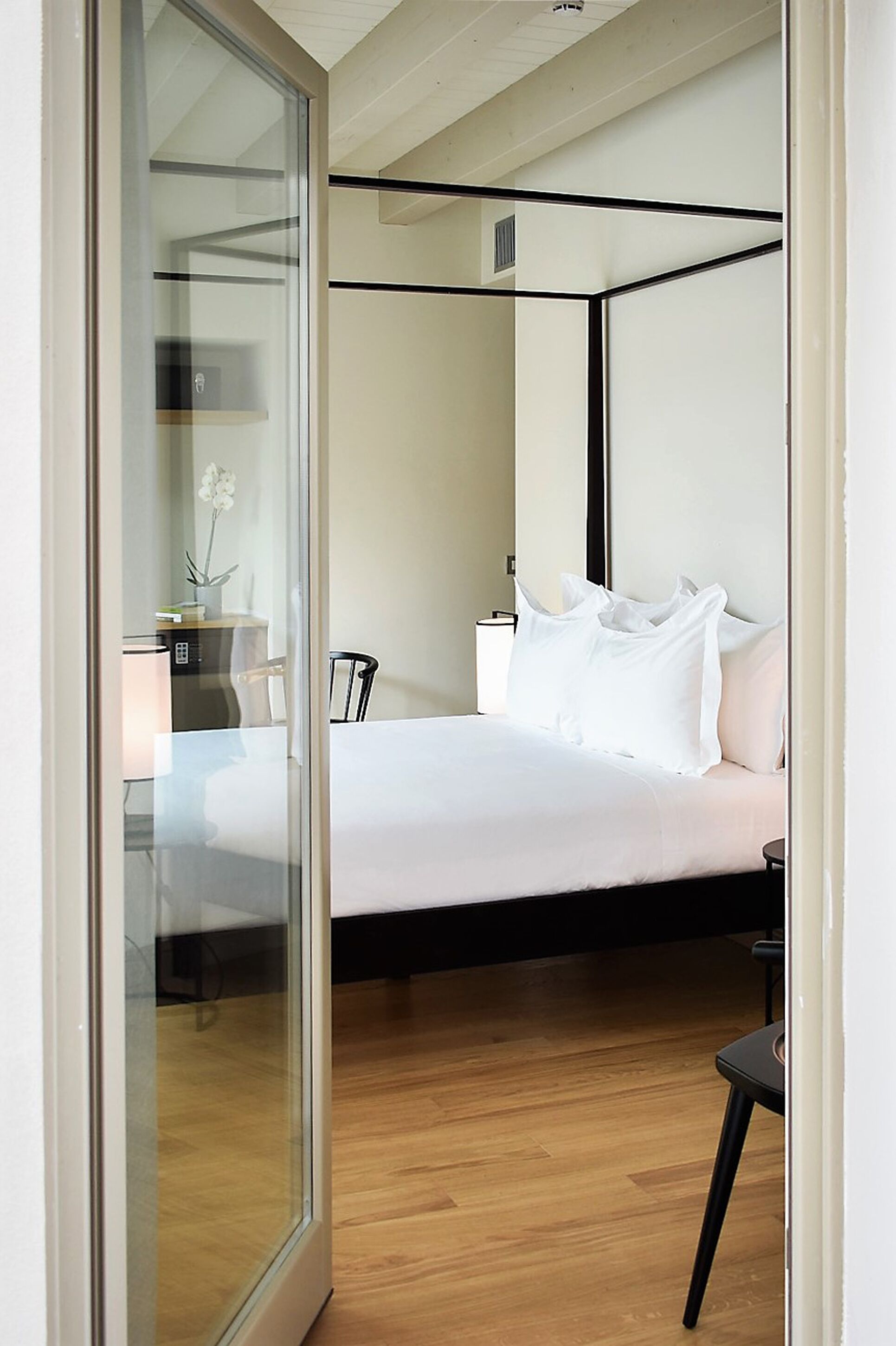 A bedroom with a four-poster bed, a desk with a chair, and a small table with a lamp.