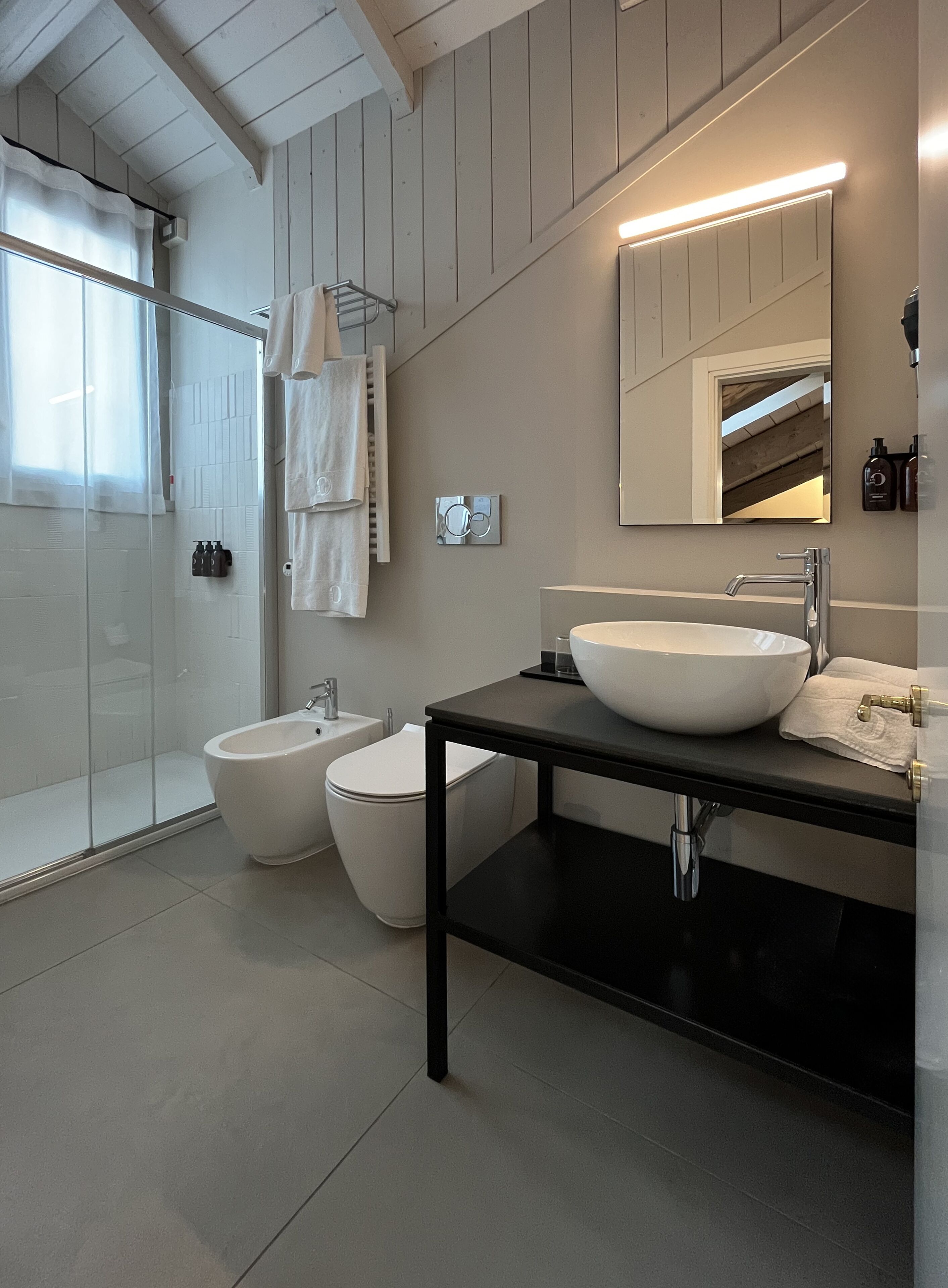 A modern bathroom with a large white sink, a bidet, and a glass shower enclosure.