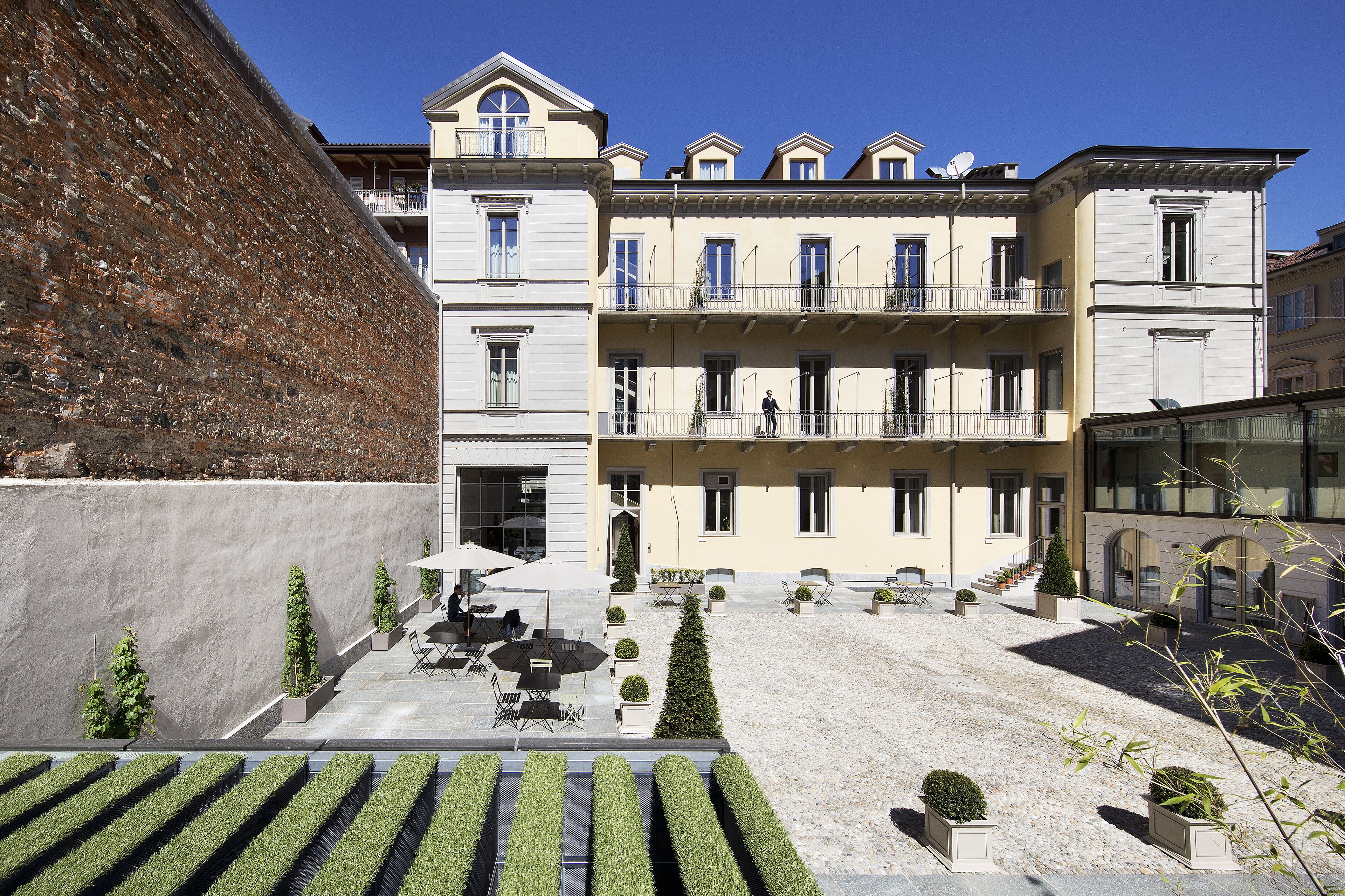 A courtyard with a building featuring multiple balconies, outdoor seating, and neatly trimmed hedges.