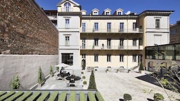 A courtyard with a building featuring multiple balconies, outdoor seating, and neatly trimmed hedges.
