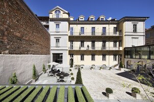 A courtyard with a building featuring multiple balconies, outdoor seating, and neatly trimmed hedges.