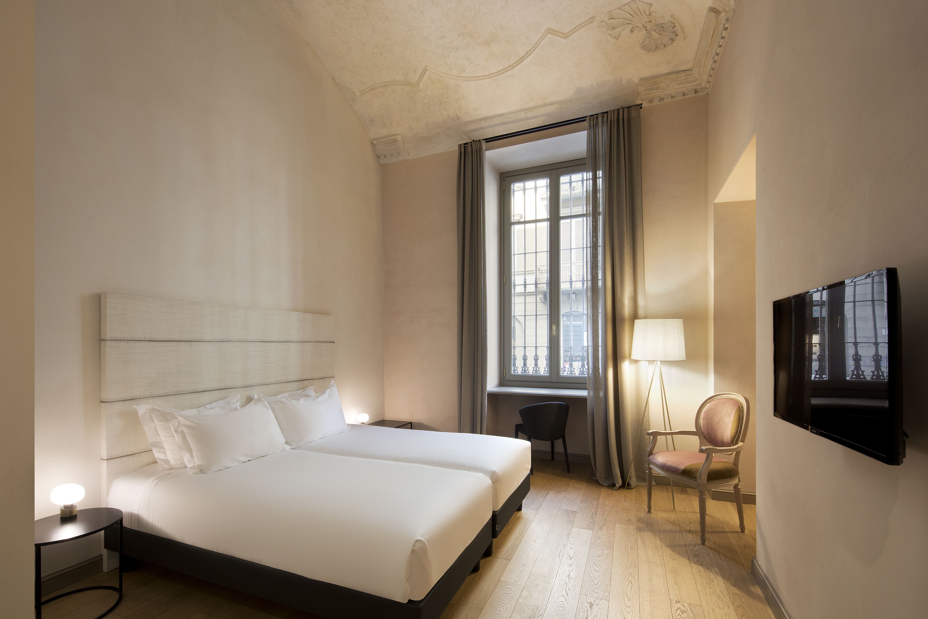 Une chambre d’hôtel avec un grand lit, un bureau, une chaise, une télévision et une fenêtre avec des rideaux.