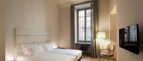 Une chambre d’hôtel avec un grand lit, un bureau, une chaise, une télévision et une fenêtre avec des rideaux.