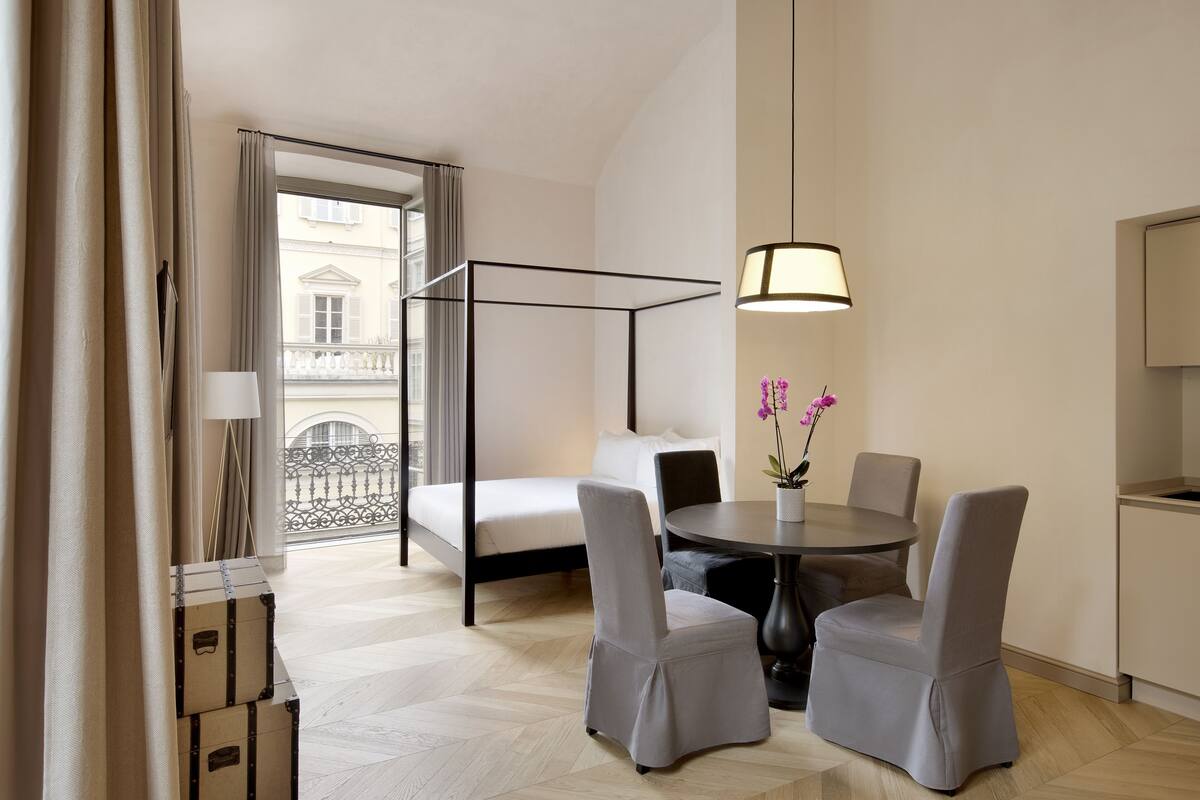 Et moderne hotelværelse med balkon, seng, spisebord med stole og en hængende lampe.