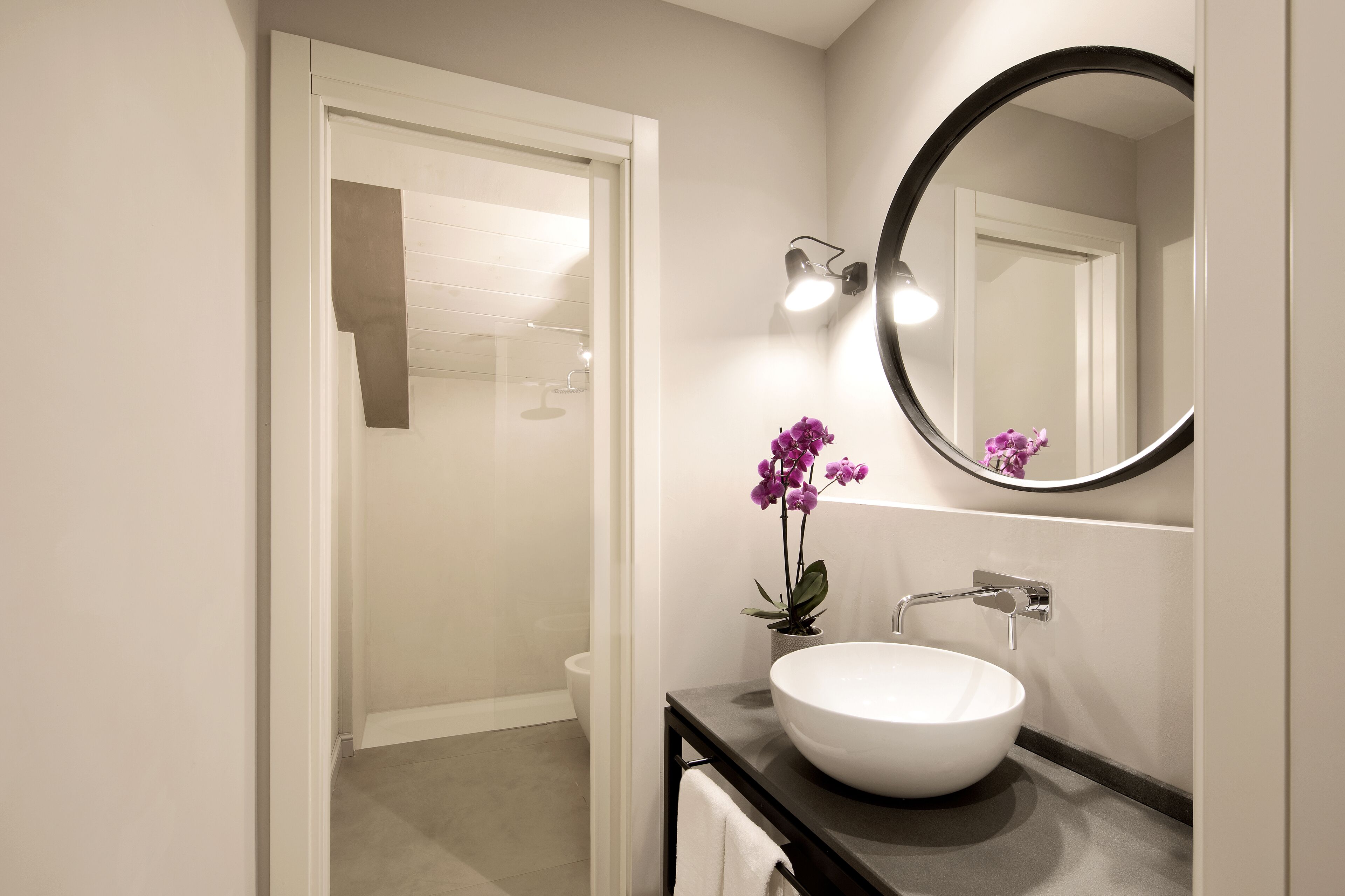 Een moderne badkamer met een witte wasbak, een ronde spiegel en een potorkidee.