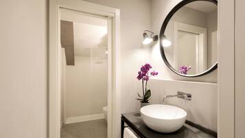 Een moderne badkamer met een witte wasbak, een ronde spiegel en een potorkidee.