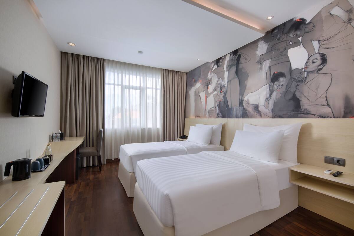A hotel room with two beds, a TV, a desk, and a large abstract painting on the wall.