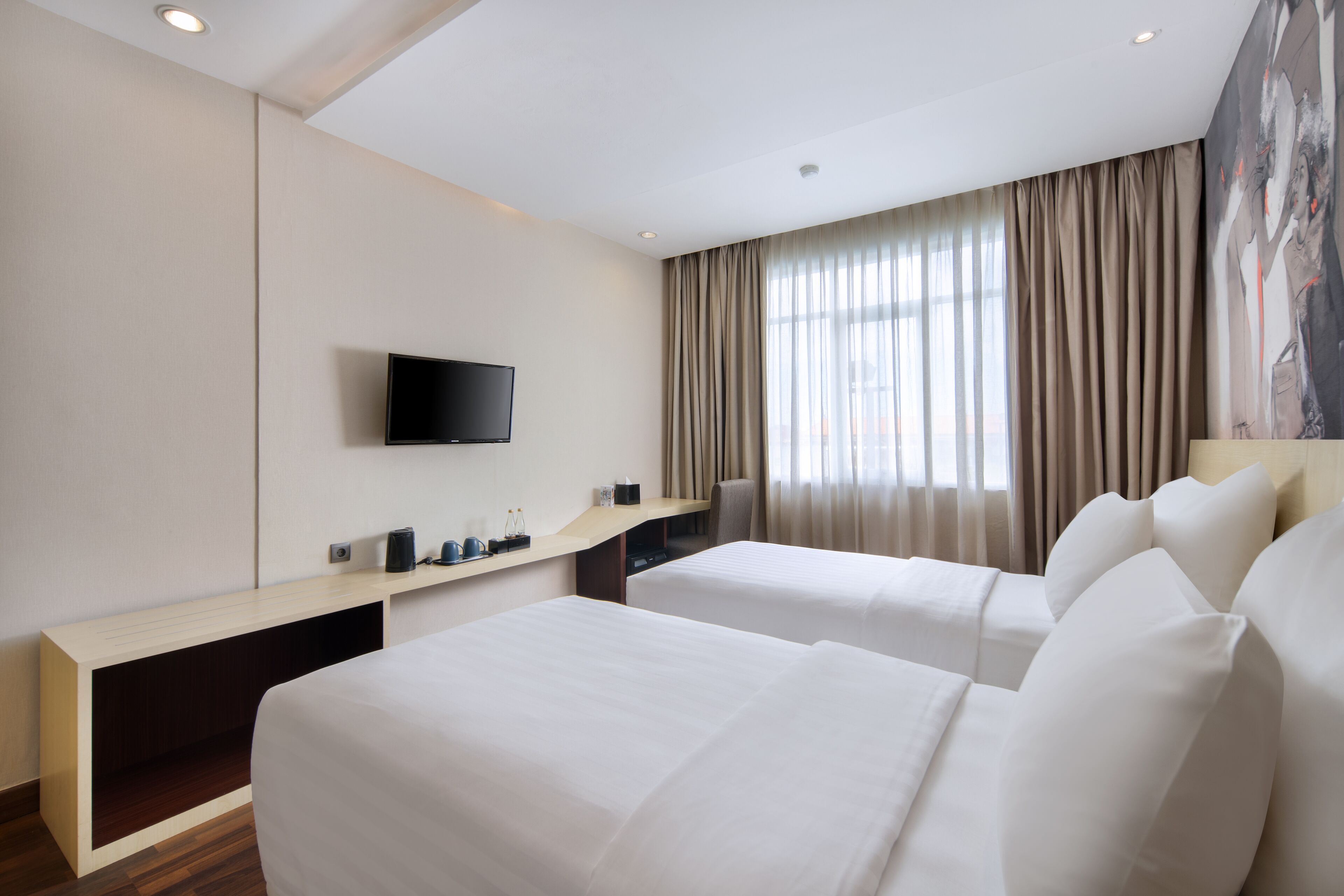 Quarto de hotel com duas camas, uma televisão na parede, uma mesa com cadeira e uma janela grande com cortinas.
