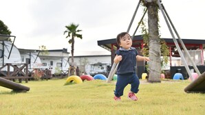 A child playing in a grassy area with playground equipment and a wooden structure in the background. - Spa Franping Village Omuta - Caravan park (Omuta)