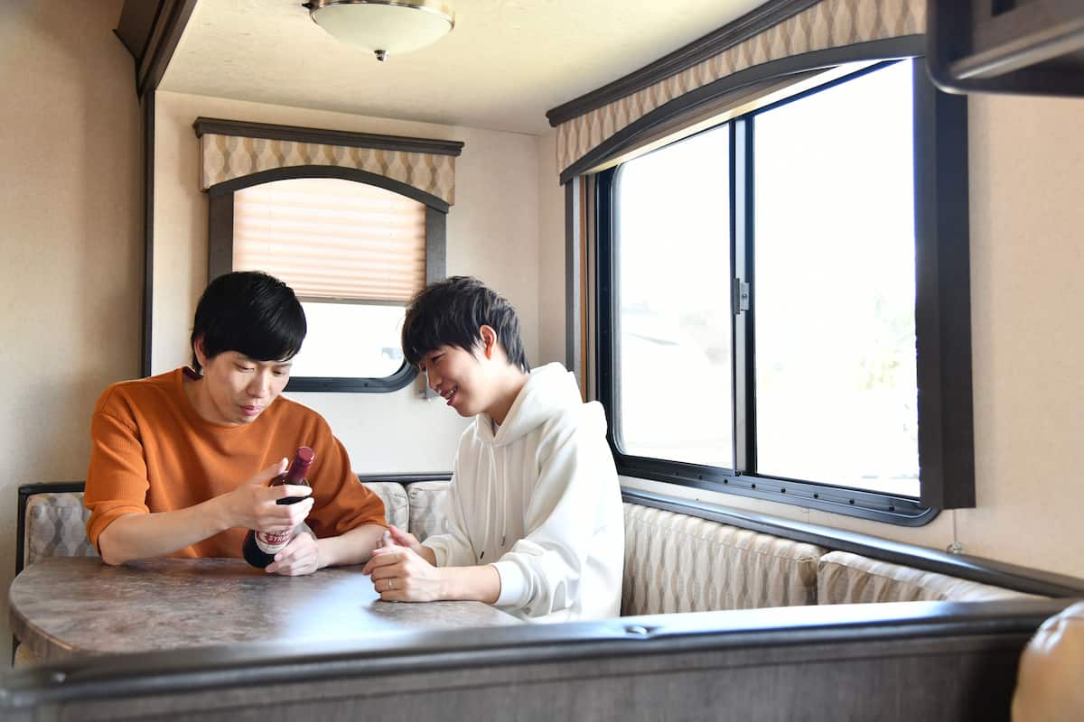 Two people seated at a table inside a vehicle with a window and a radiator.