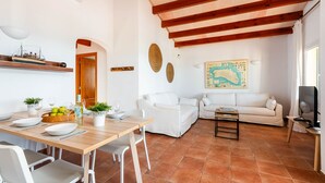 A spacious living area with a wooden dining table, white sofas, and a television.