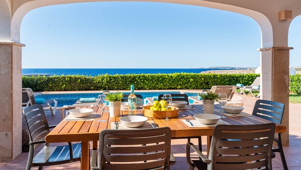A dining area with a view of the sea, a pool, and outdoor seating.