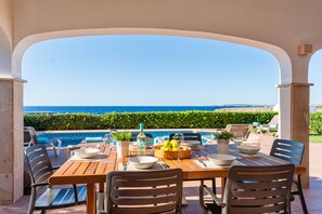 Un espace repas avec vue sur la mer, une piscine et des sièges extérieurs.
