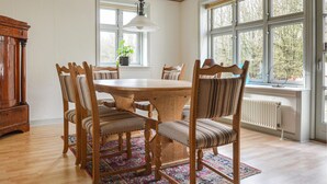 Ein Essbereich mit Holztisch und Stühlen, einem gemusterten Teppich und großen Fenstern mit Blick auf Bäume.