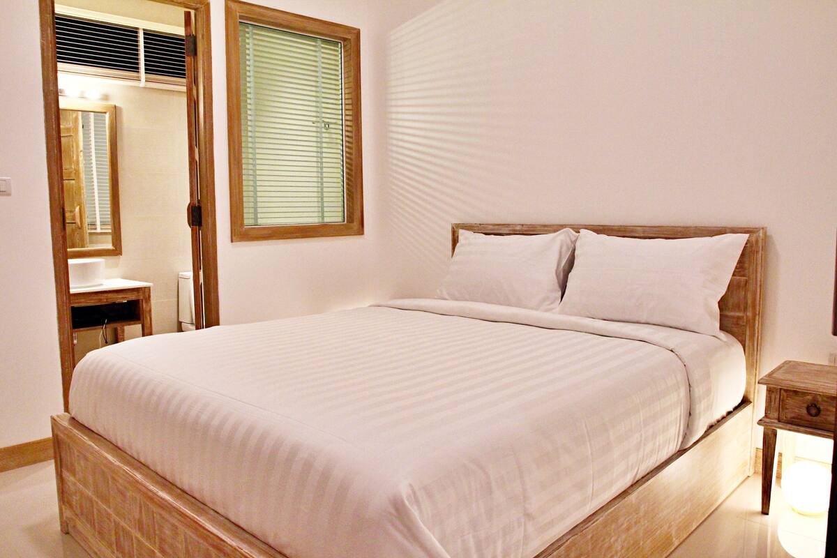 Une chambre à coucher avec un lit en bois, du linge de lit blanc, une table de chevet et un miroir.