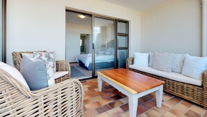 A balcony with wicker furniture, a wooden table, and a white sofa. - Blouberg Bliss - Beach Condo (Cape Town)