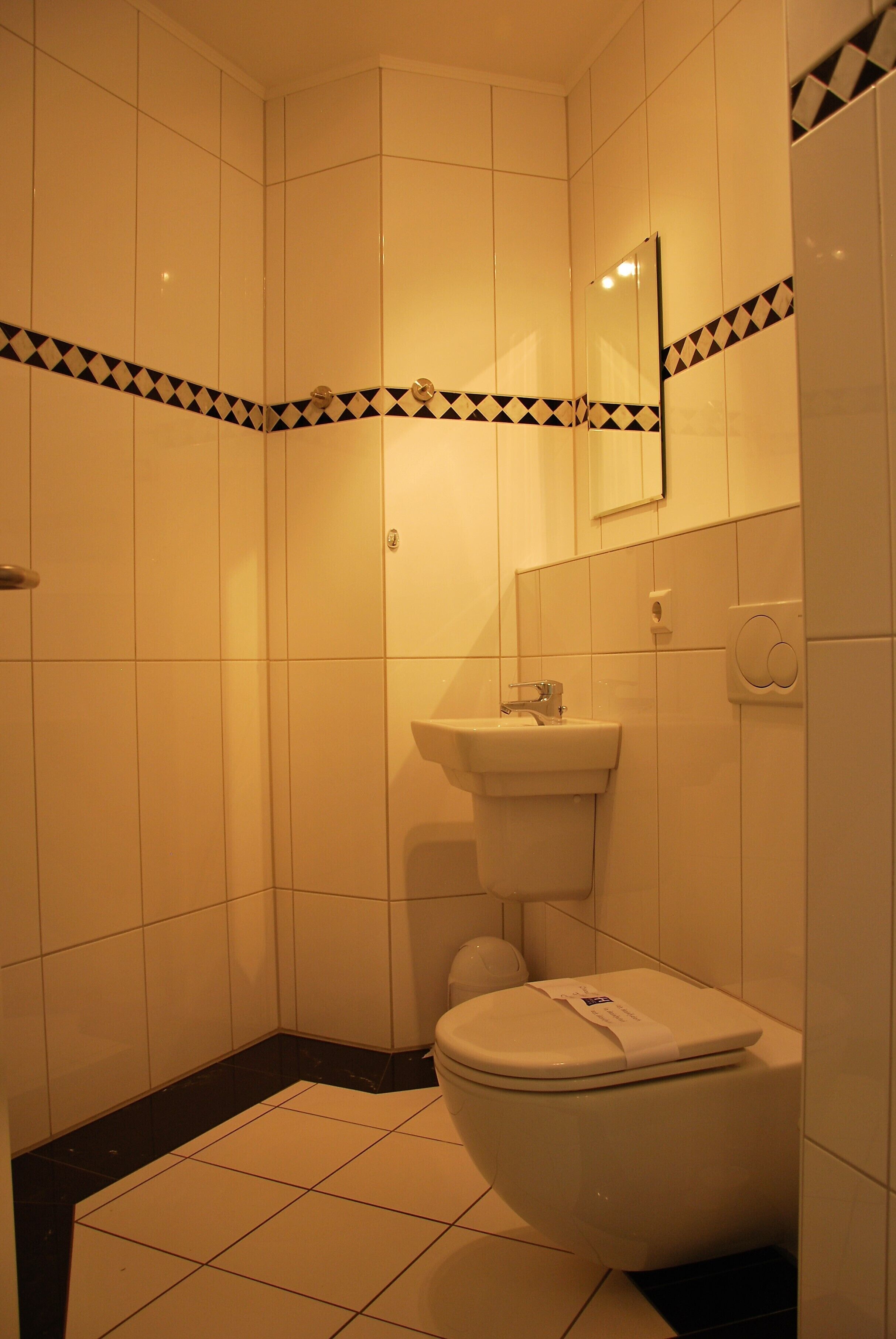 Un baño con azulejos blancos, un borde estampado en blanco y negro, un lavamanos y un inodoro.