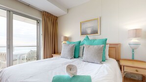 A hotel room with a bed, a view of the sea, a painting on the wall, and a window with curtains. - Sea the Mountain (Cape Town)