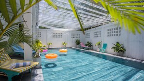 An indoor swimming pool with clear blue water, surrounded by lounge chairs and potted plants. - Golden Star Villa Hoi An (Da Nang)