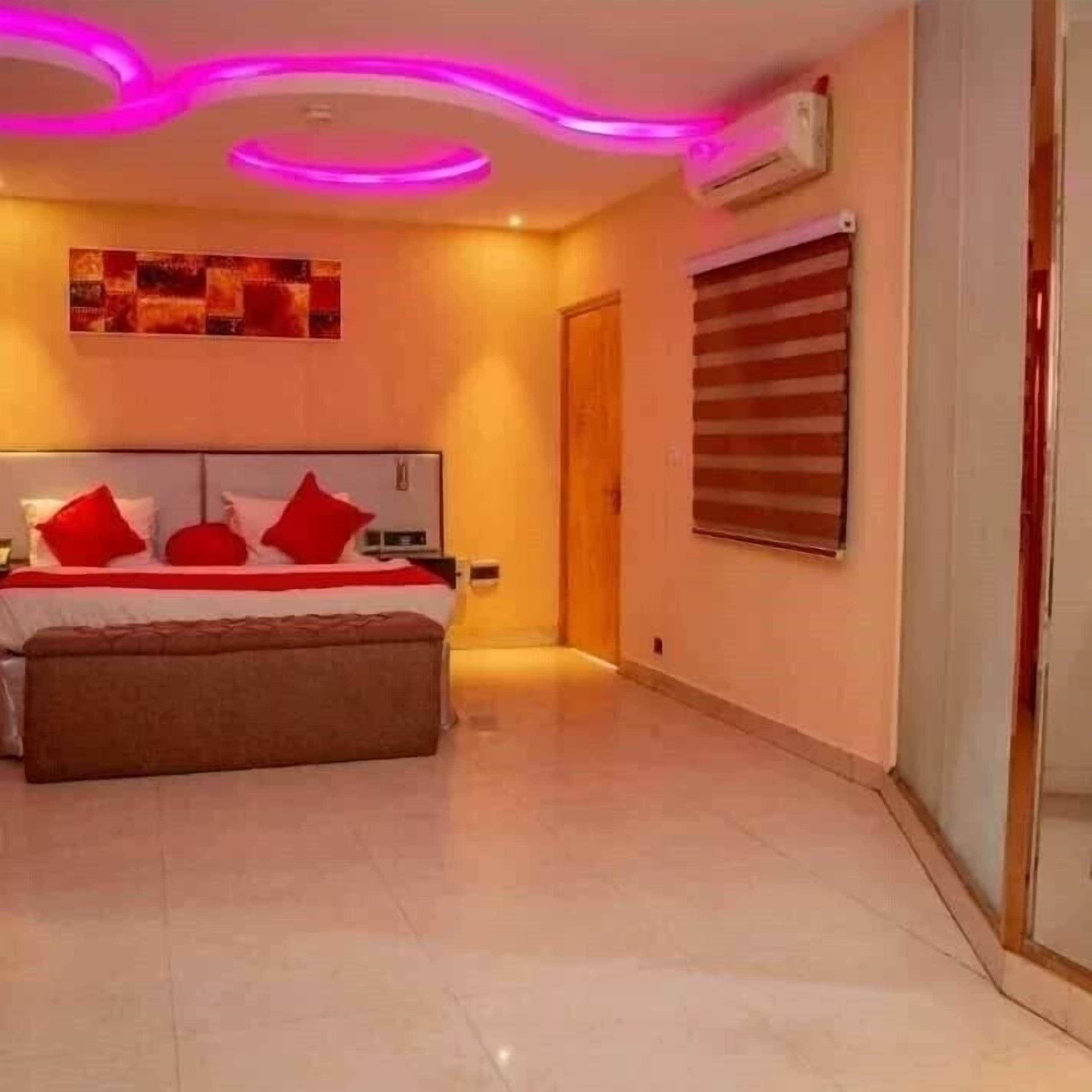 Un dormitorio con cama, mesita de noche, banco, aire acondicionado montado en la pared y ventana con persianas.
