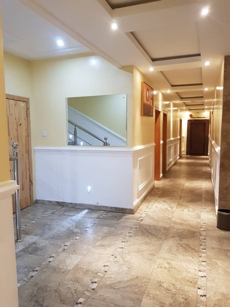 A hallway with a marble floor, a white baseboard, a wooden door, and a staircase with a handrail.